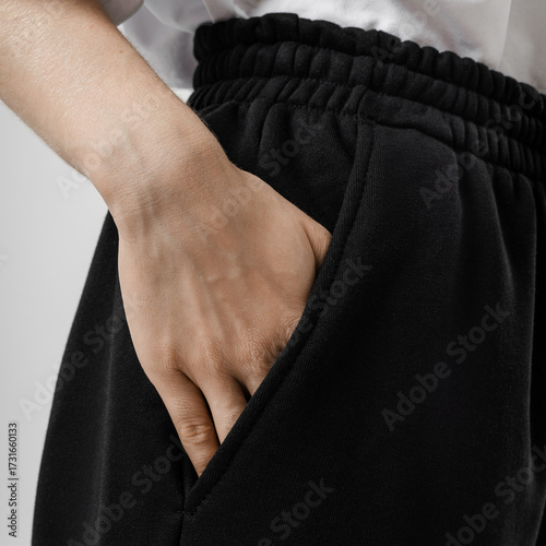 Close-up of a woman’s hand in pocket of black sweatpants against neutral studio backdrop, showing texture and detail.