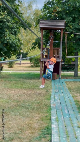 Girl in orange helmet and safety harness riding a zip line in outdoor rope adventure park