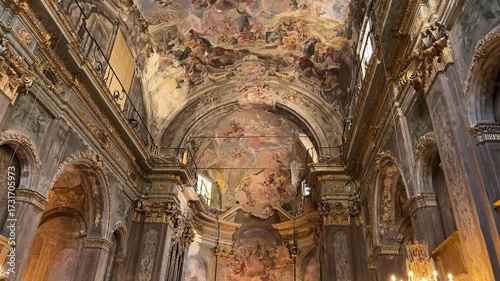 Tilt up shot exploring the ornate Baroque interior and frescoed ceiling of a historic Catholic church softly lit by warm candles in Savona, Italy.