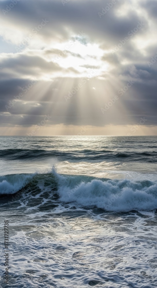 Obraz premium Sunbeams pierce through clouds over ocean waves, creating ethereal light