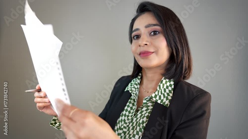 Closeup of happy successful young businesswoman manager leader boss worker looking at camera hold document and pen reading checking project information, isolated over grey background.