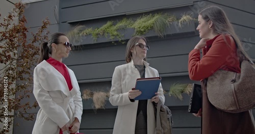 Wallpaper Mural Three businesswomen in stylish coats discuss work outside a modern office building. One holds a tablet and explains something to her colleagues. Torontodigital.ca