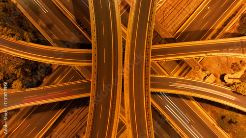 Aerial drone slow shutter night shot of illuminated multilevel junction motorway with light traffic crossing urban cityscape