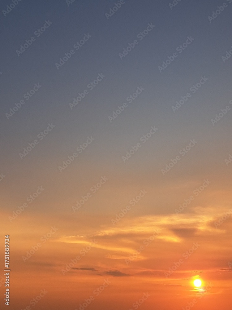 Fototapeta premium Evening sunset with an orange blue sky – White and grey clouds illuminated by the last remaining rays of the bright orange evening sun, amidst a darkening blue sky.