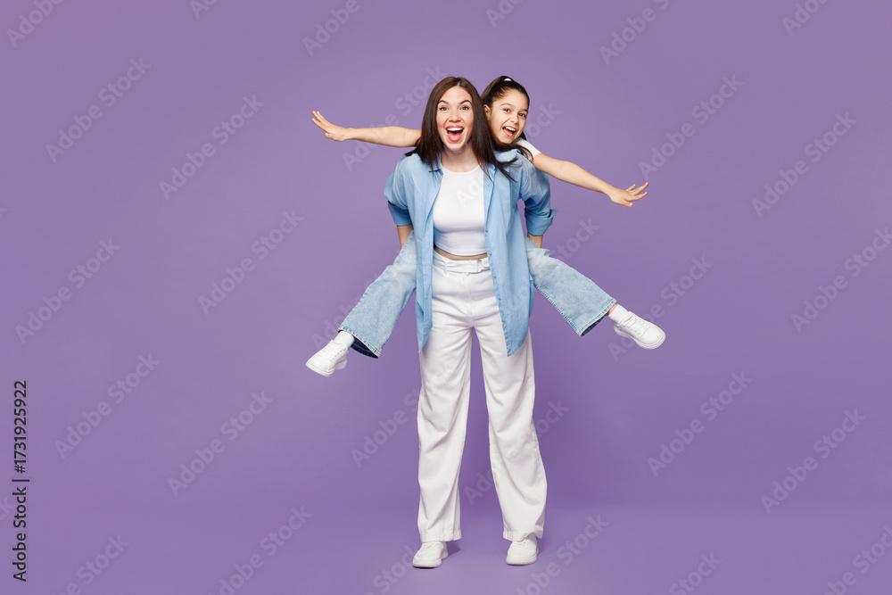 Obraz premium Full body young woman child baby girl 8-9 years old wear blue clothes. Mommy little kid daughter give piggyback ride to joyful, sit on back isolated on plain purple background. Mother's Day concept.
