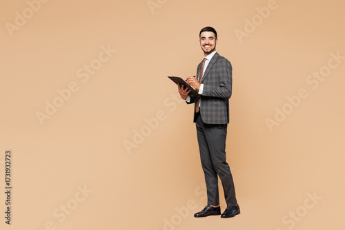 Full body young successful employee business man corporate lawyer wear classic formal grey suit shirt tie work in office hold clipboard with paper account documents isolated on plain beige background.