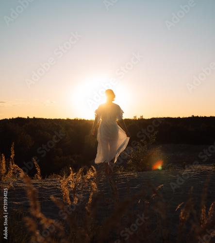 A girl in a white dress walks at sunset in summer