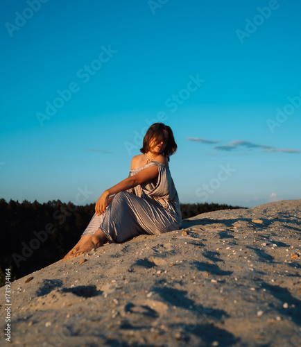 A girl in a gray dress walks on a sand dune at sunset in summer