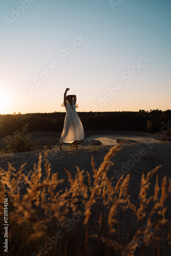 A girl in a white dress walks at sunset in summer