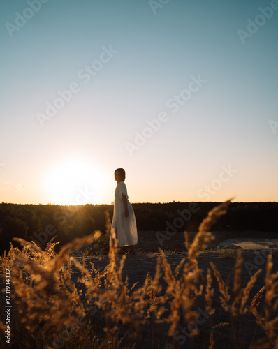 A girl in a white dress walks at sunset in summer