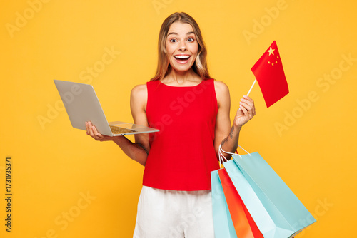 Sticker Young IT woman wear red casual clothes hold paper package bags after shopping Chinese flag use work on laptop pc computer isolated on plain orange yellow background
