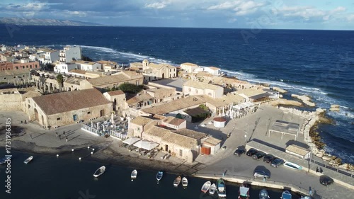 Aerial 4k drone footage of Marzamemi, Sicily, Italy, showcasing the charming coastal village, turquoise sea, fishing port, historic buildings, and scenic Mediterranean coastline