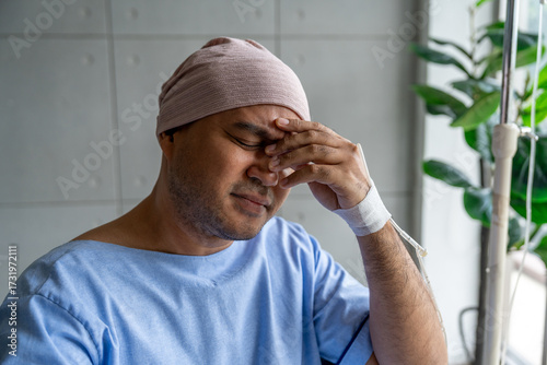 Asian male cancer patient sits in a wheelchair with an IV drip stress and sadness reflecting the emotional burden of illness. Man receiving IV treatment in a wheelchair looking tired and depressed