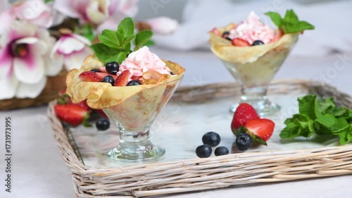 French crepes filled with whipped cream with strawberries and blueberries, strawberry syrup. Served in a glass and garnished with mint. Horizontal video. Slow motion from left to right in an arc