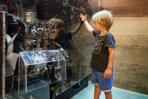 Young boy looking at transparent car engine display in science or technology museum. Educational moment exploring mechanical parts. Learning, curiosity, engineering, childhood development, school trip