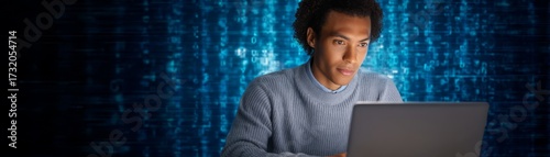 Man at Laptop Against Blue Backdrop Individual concentrating at laptop device Plain blue backdrop provides clean professional setting.