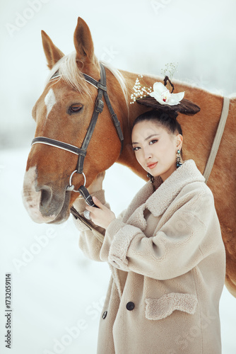 Young stylish asian woman in vintage outfit standing close to a brown horse