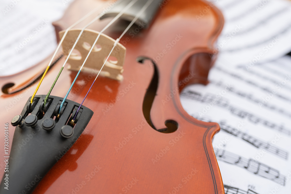 Fototapeta premium Close-up view of a wooden violin resting on sheet music, showcasing intricate details of the instrument's body and strings, creating a harmonious blend of music and craftsmanship