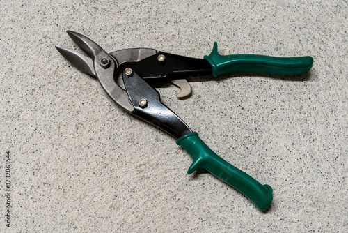 Photos Pair of tin snips, opened, with green grips, on a concrete textured background