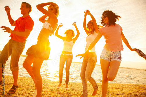 Young men and women dancing on the beach at sunset on a summer evening