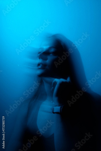 Dreamy moody cinematic portrait of a brunette woman with blue-aqua glow and long exposure