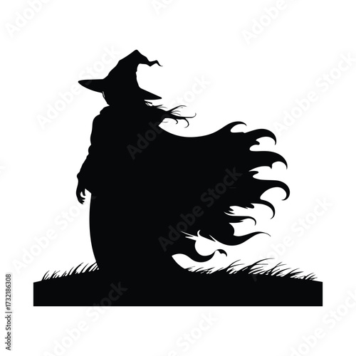 Silhouette of a witch with a flowing cape standing in grass under a full moon