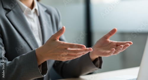 Person in a suit gesturing with their hands in front of a laptop.