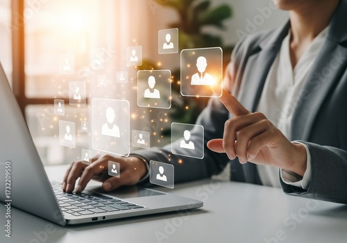 Wallpaper Mural A businesswoman in a grey suit uses a laptop at a bright desk. She is pointing at a holographic display showing a network of interconnected user profile icons. This represents Human Resources (HR) man Torontodigital.ca