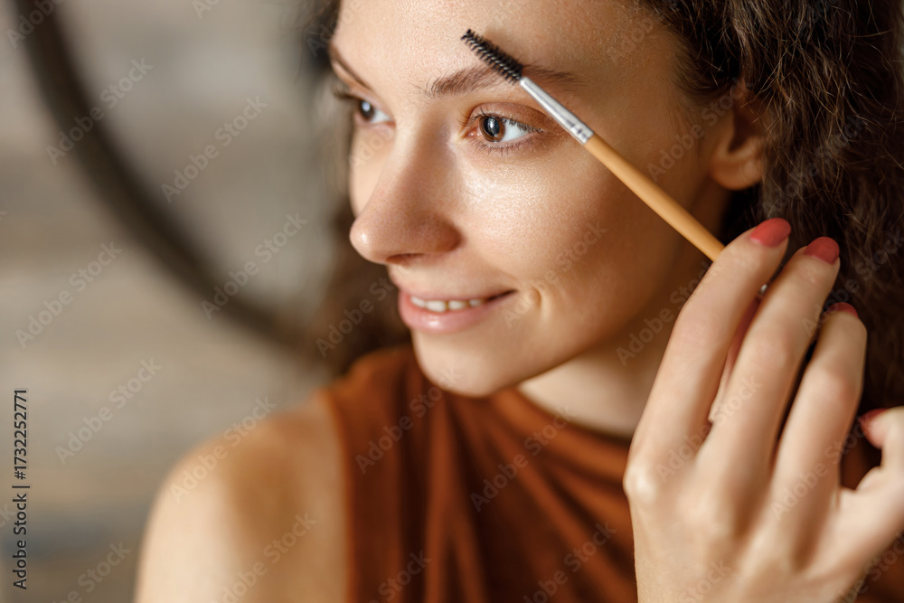 Obraz premium In a warm and inviting setting, a young woman skillfully enhances her eyebrows with precision and care