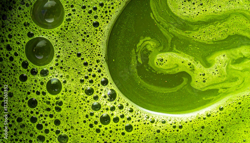 The image presents a close up view of a bright green liquid filled with bubbles of varying sizes. The liquid appears to be thick and viscous, exhibiting swirling patterns and textures