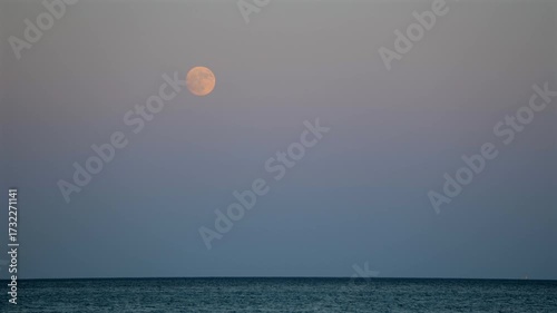 A tranquil time lapse scene capturing a magnificent moonrise over the calm sea, with a solitary boat anchored in the foreground, offering a peaceful and reflective atmosphere.