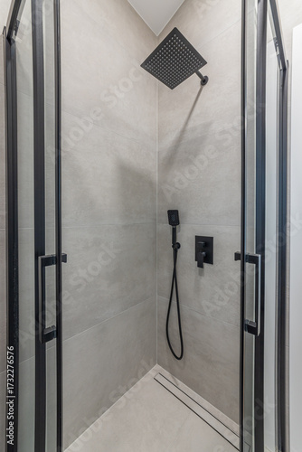 Stylish modern shower with black matte fixtures, a rainfall shower head, and gray tile. Elegant bathroom interior design for a contemporary home or hotel.