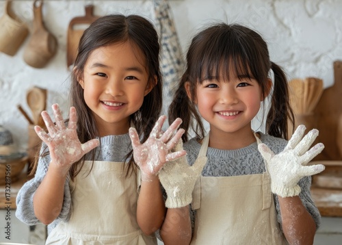 a young asian mother and daughter, wearing aprons and with their hands covered in white paper to keep the kitchen clean, stand at home for a cooking class