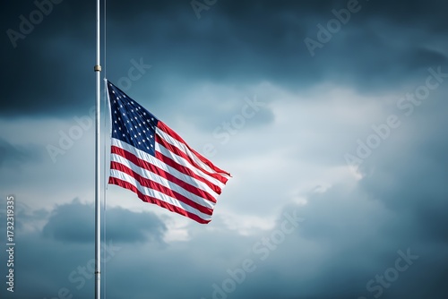 The United States flag waves at half mast against a cloudy sky.