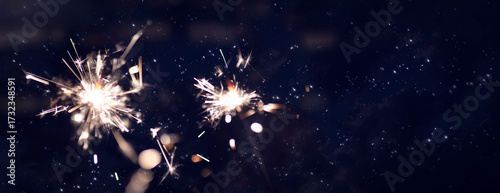 Dark night sky with glowing sparklers and golden bokeh. Horizontal background for christmas and new year with space for text. New year's eve fireworks.