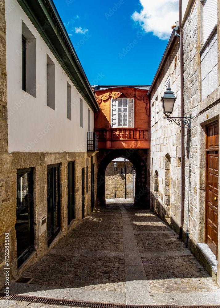 Fototapeta premium A narrow street in a historic town with a wooden bridge connecting buildings.