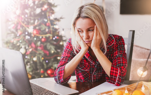 Sad middle aged woman working at the home office by laptop during Christmas holiday