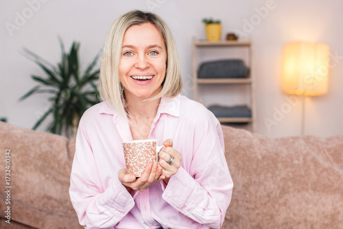 Adult woman sitting on the sofa at home and having a cup of coffee