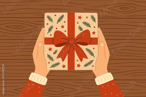 Hands holding a Christmas gift box with a red bow on a wooden table. Top view. Concept of giving and receiving presents during the winter holidays, Xmas, and New Year celebration.