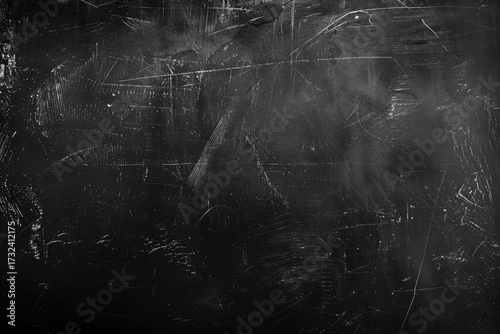 A dark, heavily textured surface with numerous light gray scratches and marks creating an abstract pattern.  The background is predominantly black, fading slightly at the edges