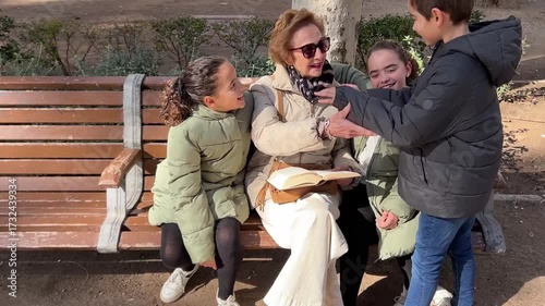 Grandmother storytelling to granddaughters on a park bench as grandson arrives to listen and join family bonding