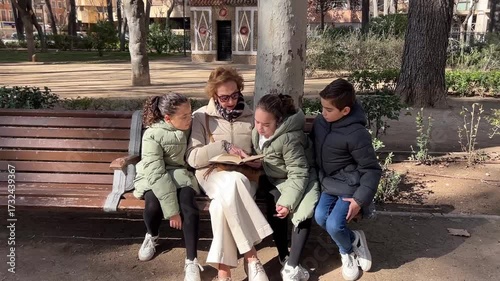 Grandmother reading to grandchildren triplets at park, enjoying outdoor family bonding and learning
