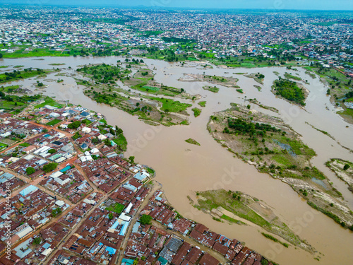 Aerial view of muddy river winding through a dense urban landscape, juxtaposing the organic flow of water against the rigid structures of Kabala Costain, Kaduna, Nigeria.