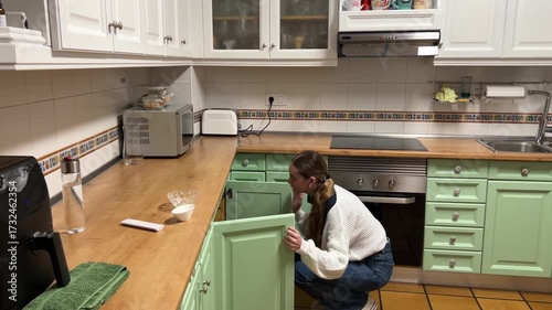 Teen girl retrieving a bag of potato chips from the kitchen cabinet to prepare a snack