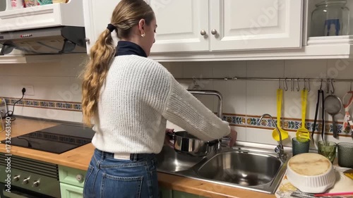 Teen girl filling a cooking pot with water under the kitchen faucet to prepare a meal