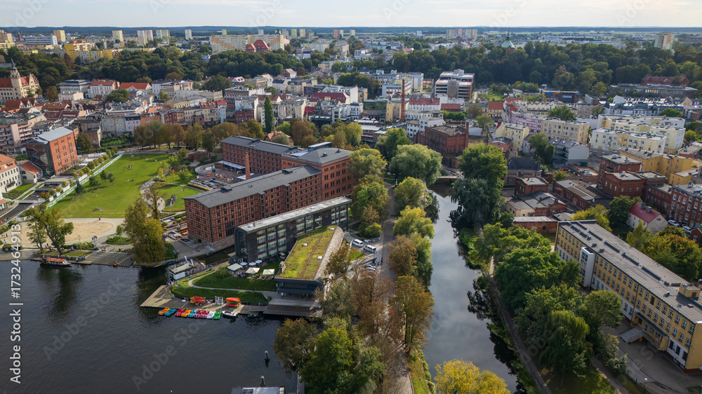 Aerial view of the contrasting textures of red brick buildings and the serene canal reflecting the sky, surrounded by lush greenery, Bydgoszcz, WojewÃ³dztwo kujawsko-pomorskie, Poland.