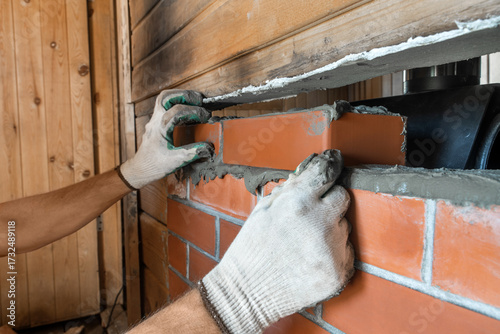 Bricklayer lays red bricks around a sauna stove. Renovation work. The bricks are laid on a refractory sand-cement mixture.