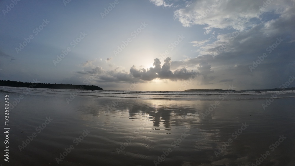 Naklejka premium Tranquil Coastal Scenery: Rhythmic Movement of the Water and Symmetrical Reflections During the Golden Hour on a Broad, Flat Beach.