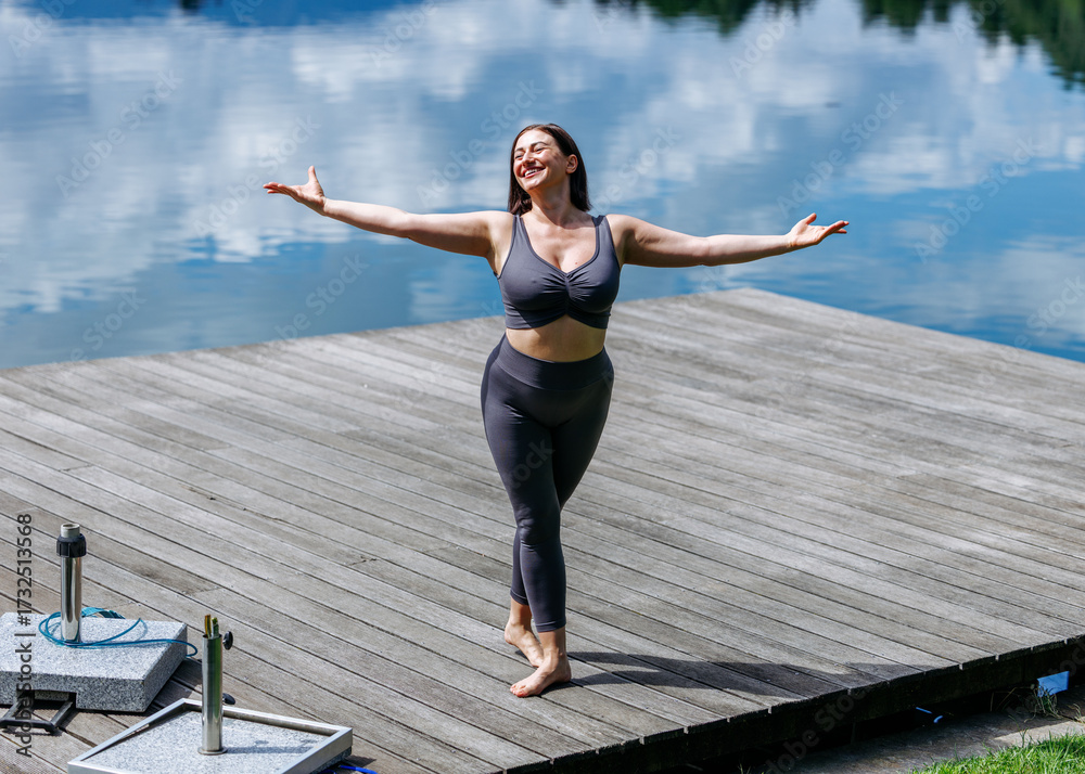 Fototapeta premium Young caucasian female practicing yoga outdoors on lakeside dock