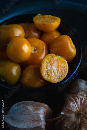 Close-up of fresh golden berries, also known as physalis or ground cherries, in a black bowl on a dark textured background.